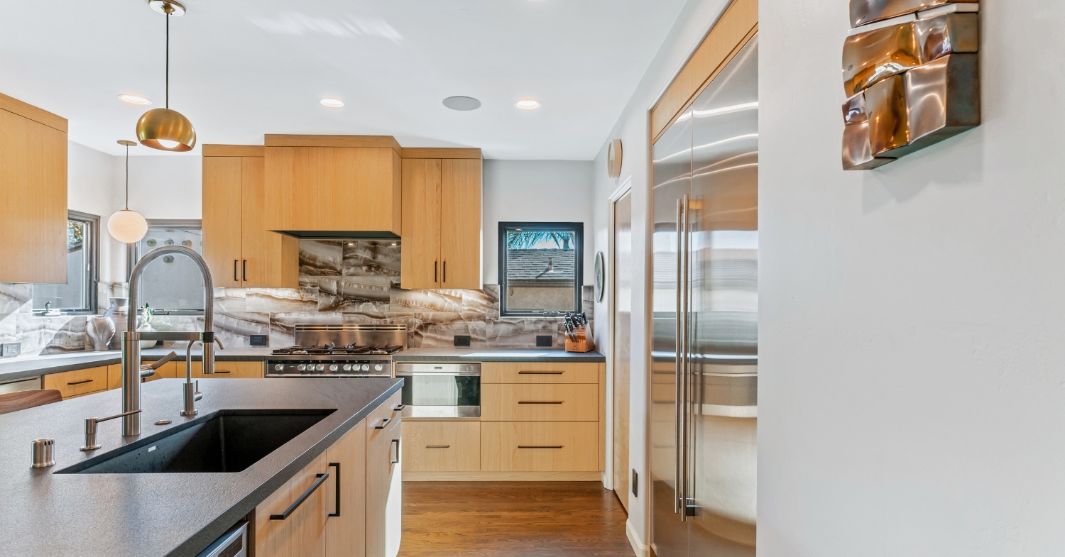 Remodeled kitchen with light maple flat-panel cabinets, dramatic onyx-look slab backsplash, professional gas range and built-in stainless refrigerator.