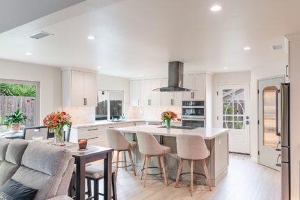 Open-concept kitchen and living area with a large island, four upholstered stools, white cabinetry, and sliding glass doors to the backyard.
