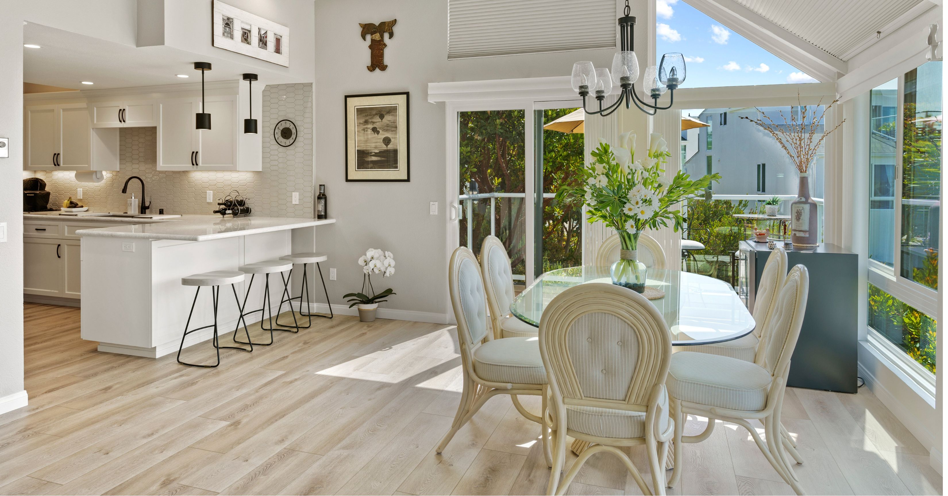 Open kitchen and dining area with white cabinetry, breakfast-bar seating, a glass table, and large windows.