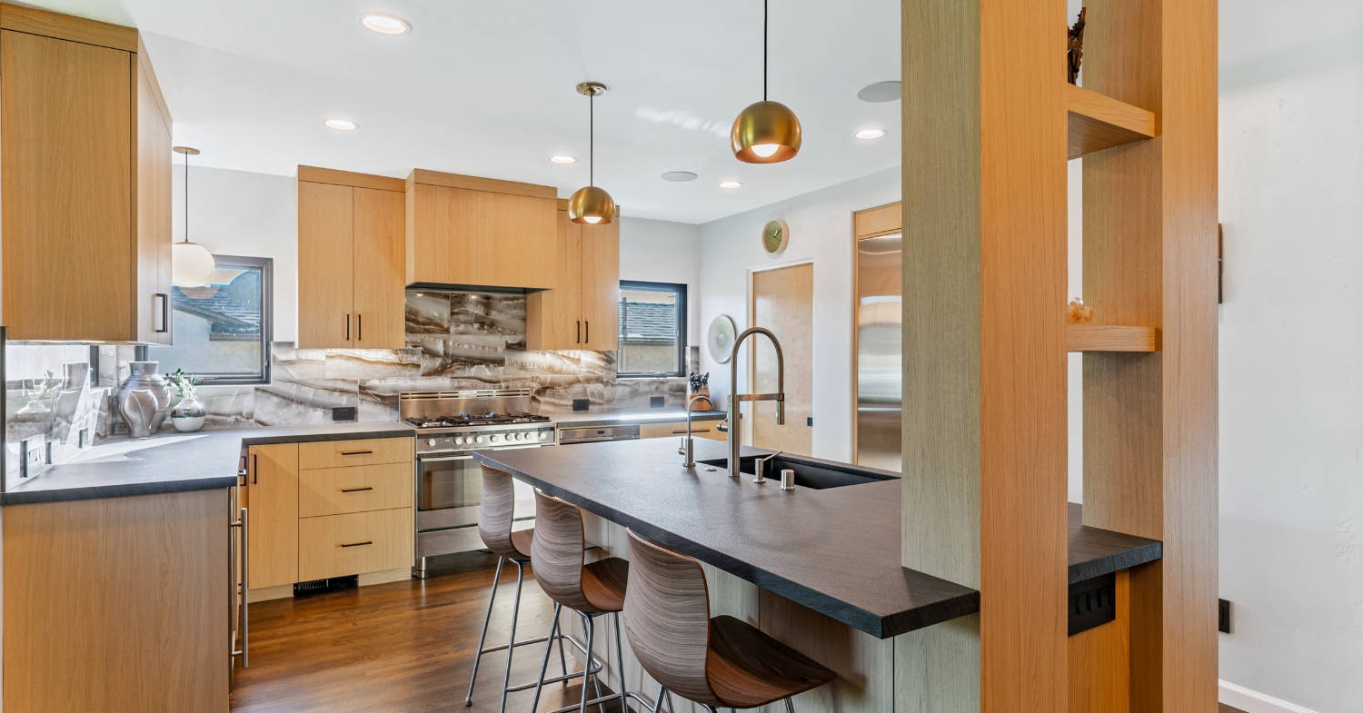 Contemporary kitchen with natural wood cabinets, dark countertops, a waterfall island, and a dramatic stone backsplash.