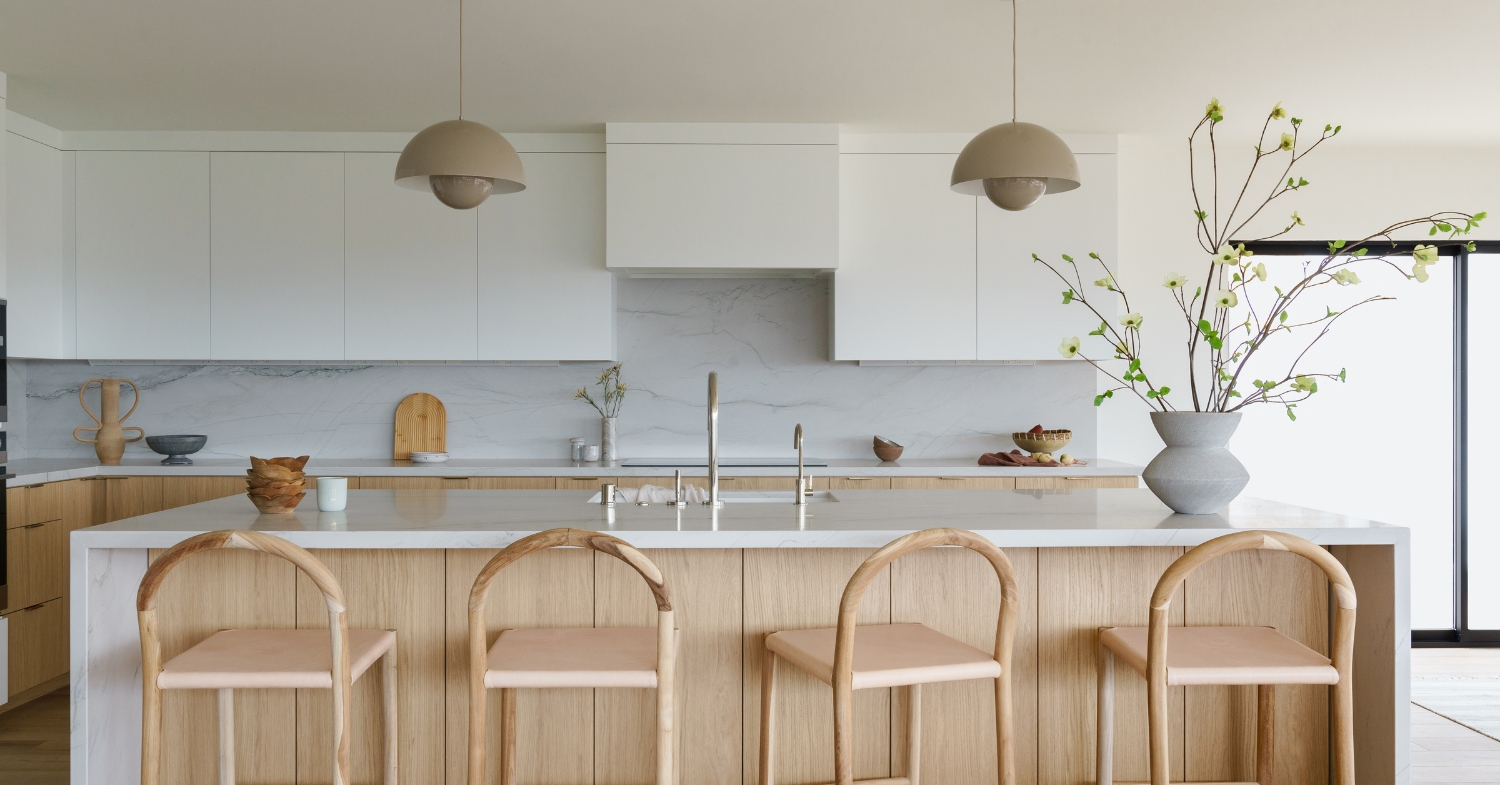 Serene modern kitchen with white oak island, marble-look waterfall counters and backsplash, arched wood counter stools and dome pendant lights.