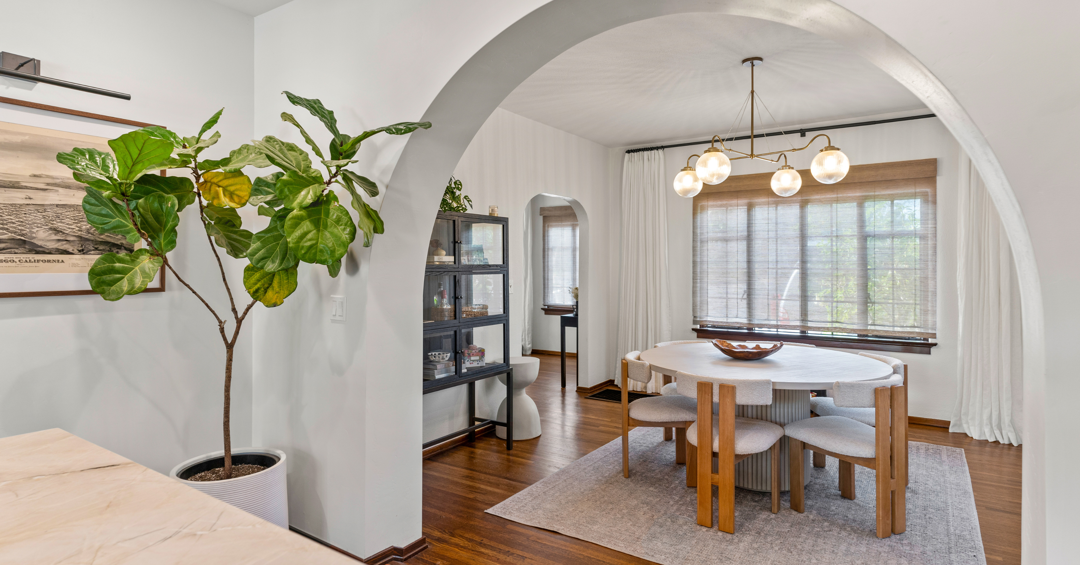 Elegant dining room featuring arched entryways, hardwood floors, large windows, modern chandelier, and contemporary furnishings after a whole-home renovation.