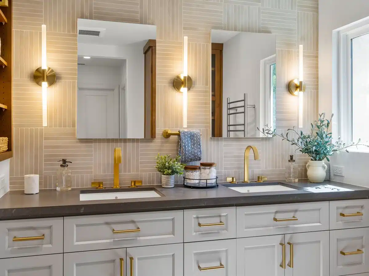 White double vanity with brass faucets, framed mirrors and wall-mounted lighting.