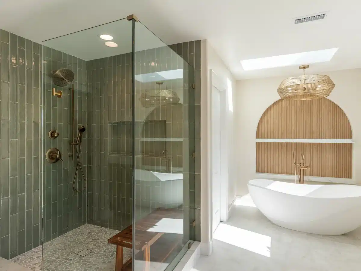 Bathroom with a green tile shower, frameless glass enclosure and a freestanding white bathtub.