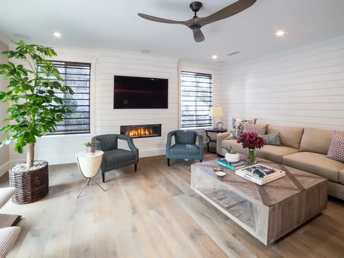 Family room with a fireplace, white wall paneling, pale wood flooring and a sectional sofa.