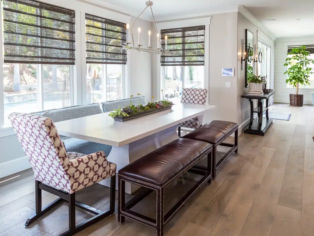 Dining area with a long wood table, upholstered chairs and windows along two walls.