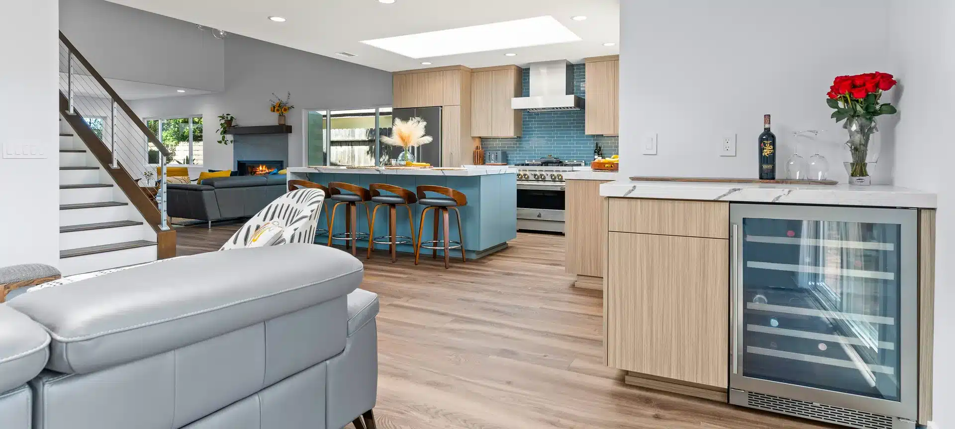 Open living area with a blue kitchen island, light wood cabinetry and a built-in beverage refrigerator.