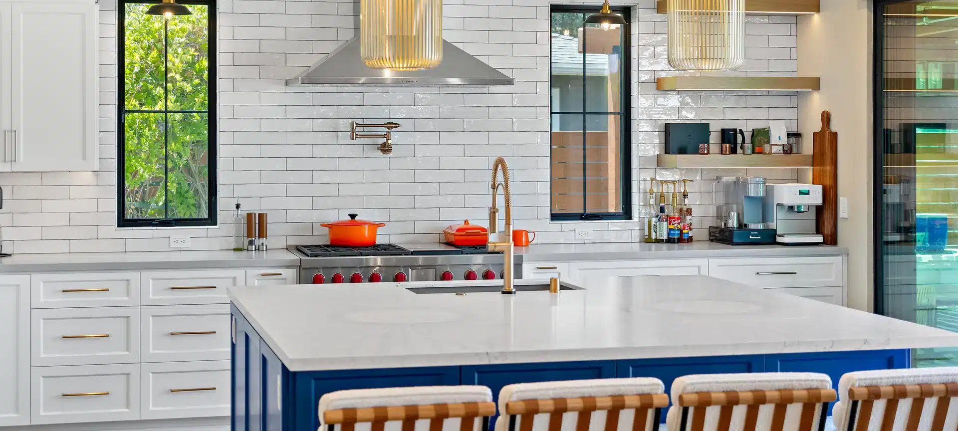 White kitchen with a blue island, brass fixtures, tall windows and pendant lighting.