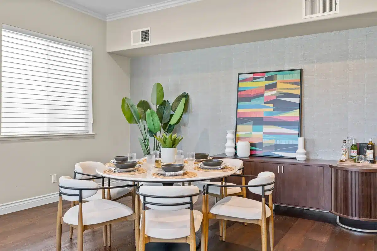 Dining room with a round table, white chairs, and a wood sideboard.