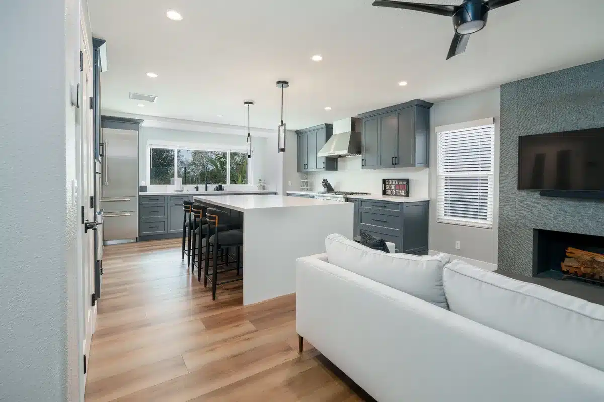 Connected kitchen and living room with gray cabinetry and wood flooring.