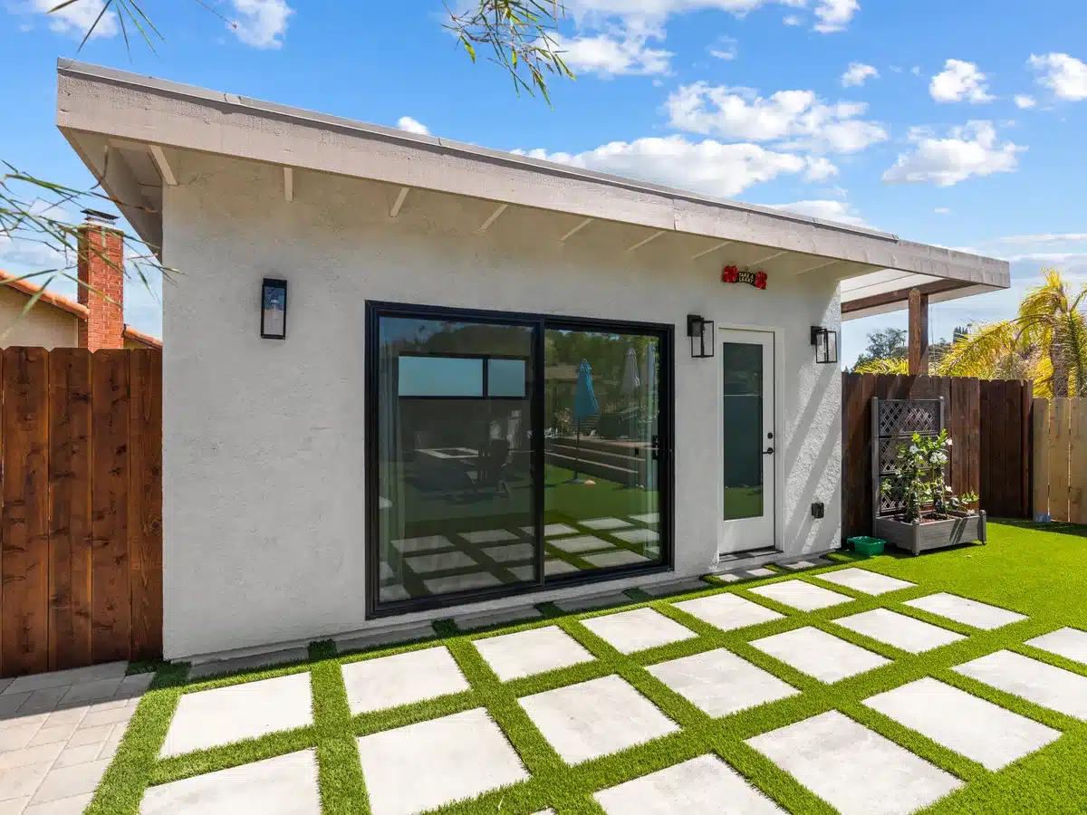 Detached backyard structure with white stucco, a sloped roof and black-framed sliding doors.