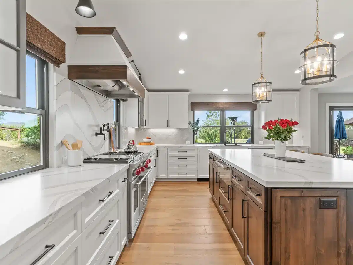 White kitchen with a wood island, stone countertops and glass pendant lights.