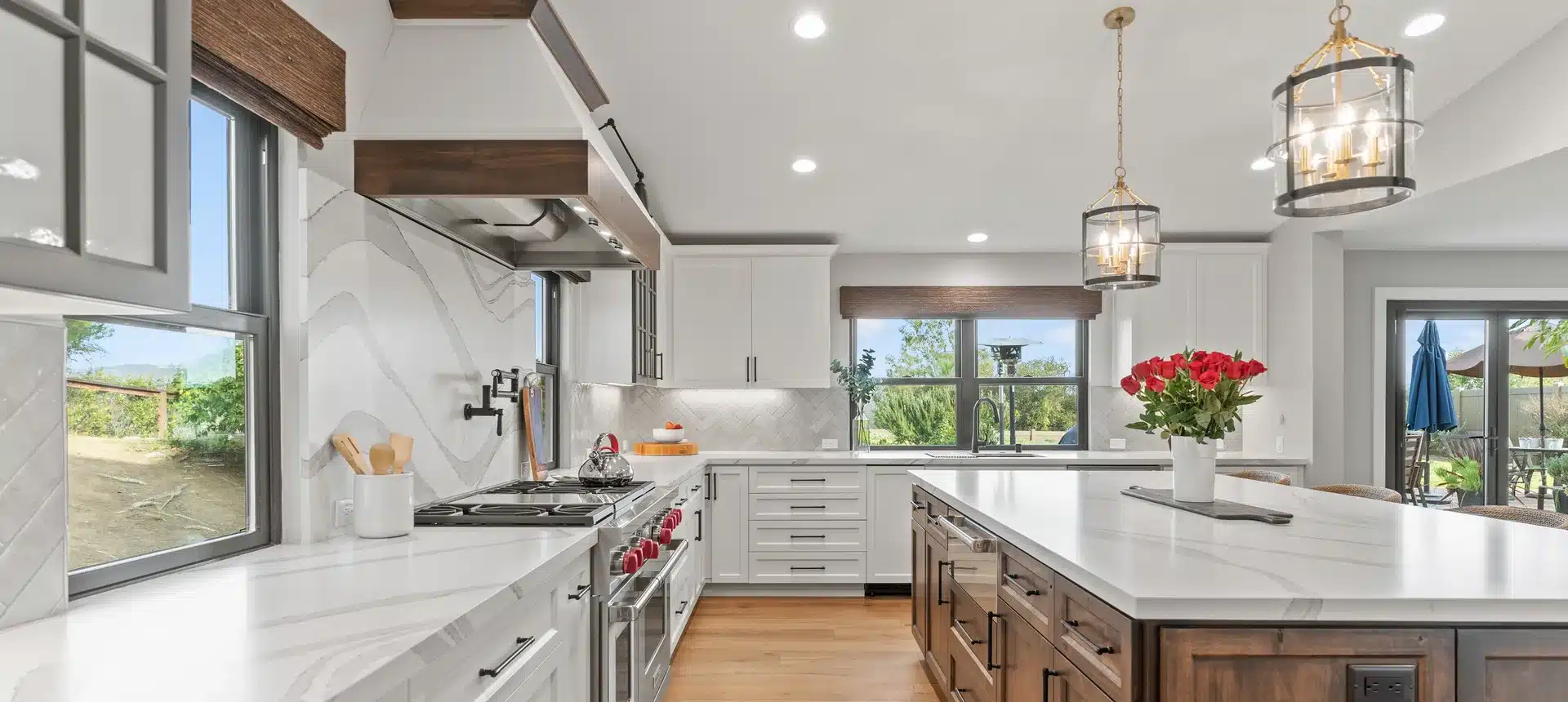 White kitchen with a wood island, stone countertops and glass pendant lights.