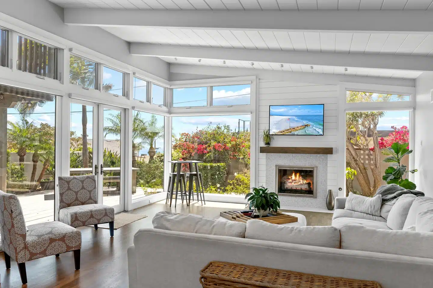La Jolla coastal living room with large windows, white beams, and a fireplace.