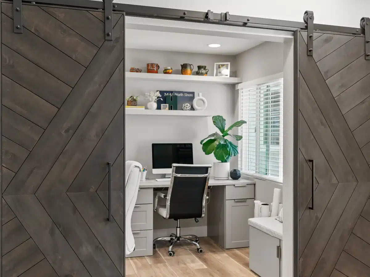 Home office with built-in shelving behind a pair of wood sliding barn doors.