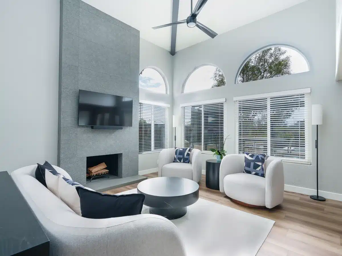 Vaulted living room with arched windows, white seating, and a tall gray fireplace.
