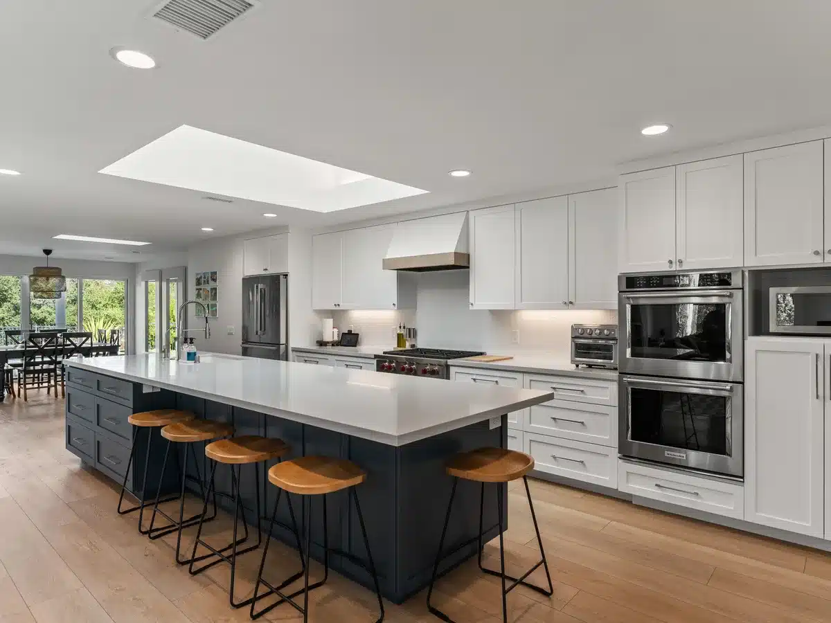 Open kitchen with a navy island, wood stools, white cabinets, and a skylight.
