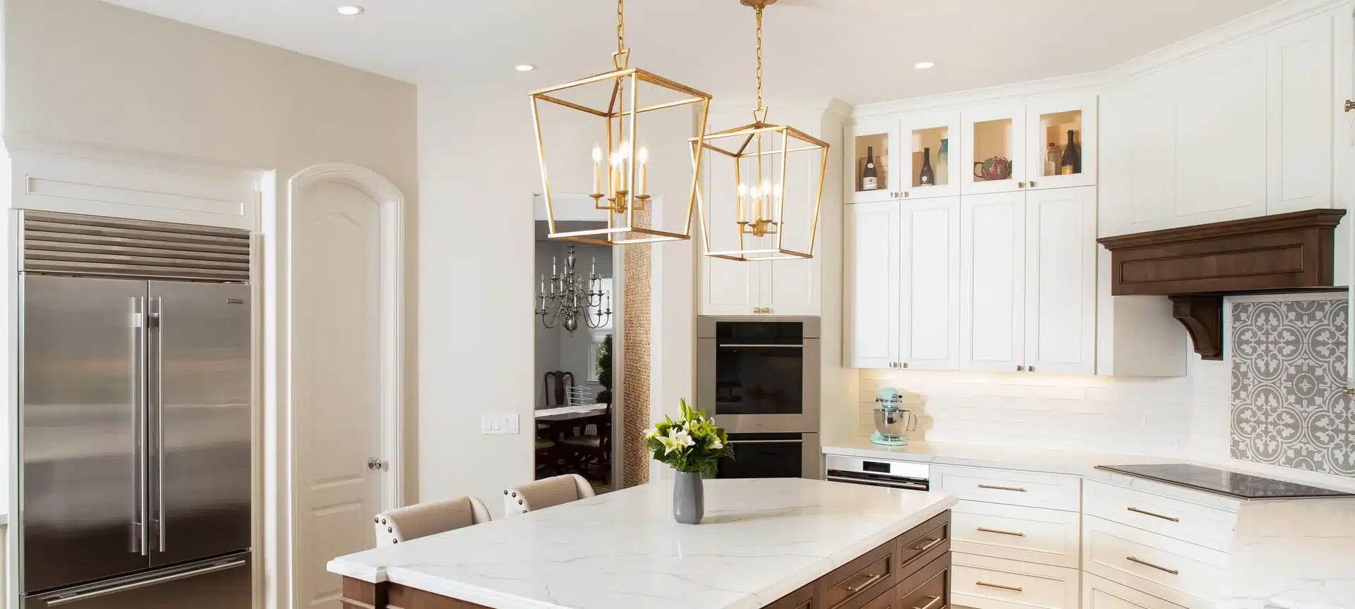 White kitchen cabinetry, a wood island with a pale countertop, and brass lantern pendant lights.