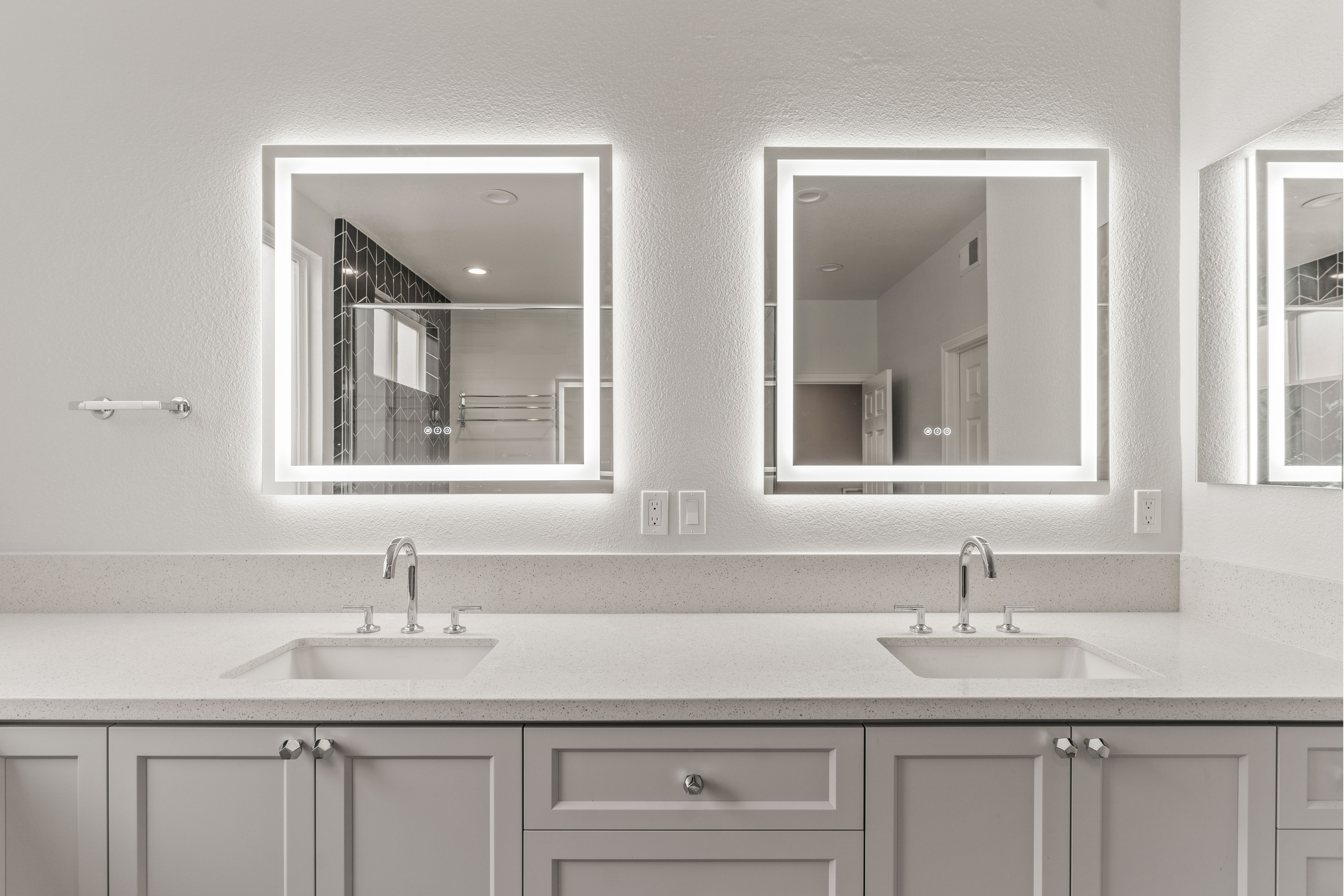 Double vanity with gray cabinetry, light counters, chrome fixtures and illuminated mirrors.