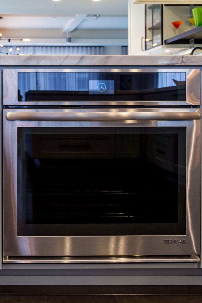 Stainless wall oven set into gray kitchen cabinetry beneath a light stone countertop.