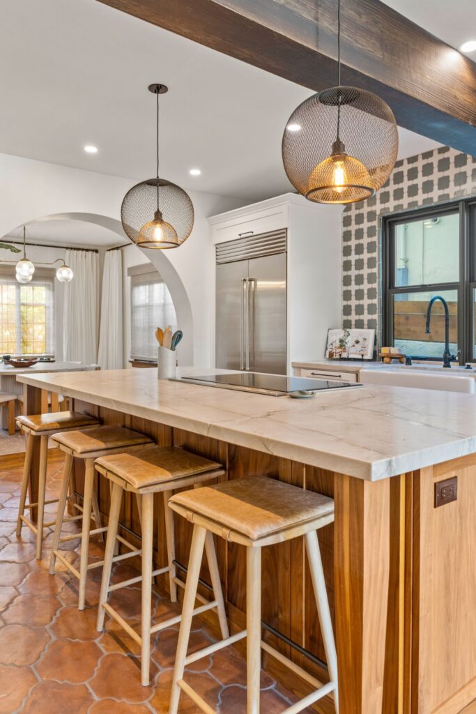 Kitchen island with wood cabinetry, white veined countertop, pendant lights, stainless refrigerator and terracotta tile floor