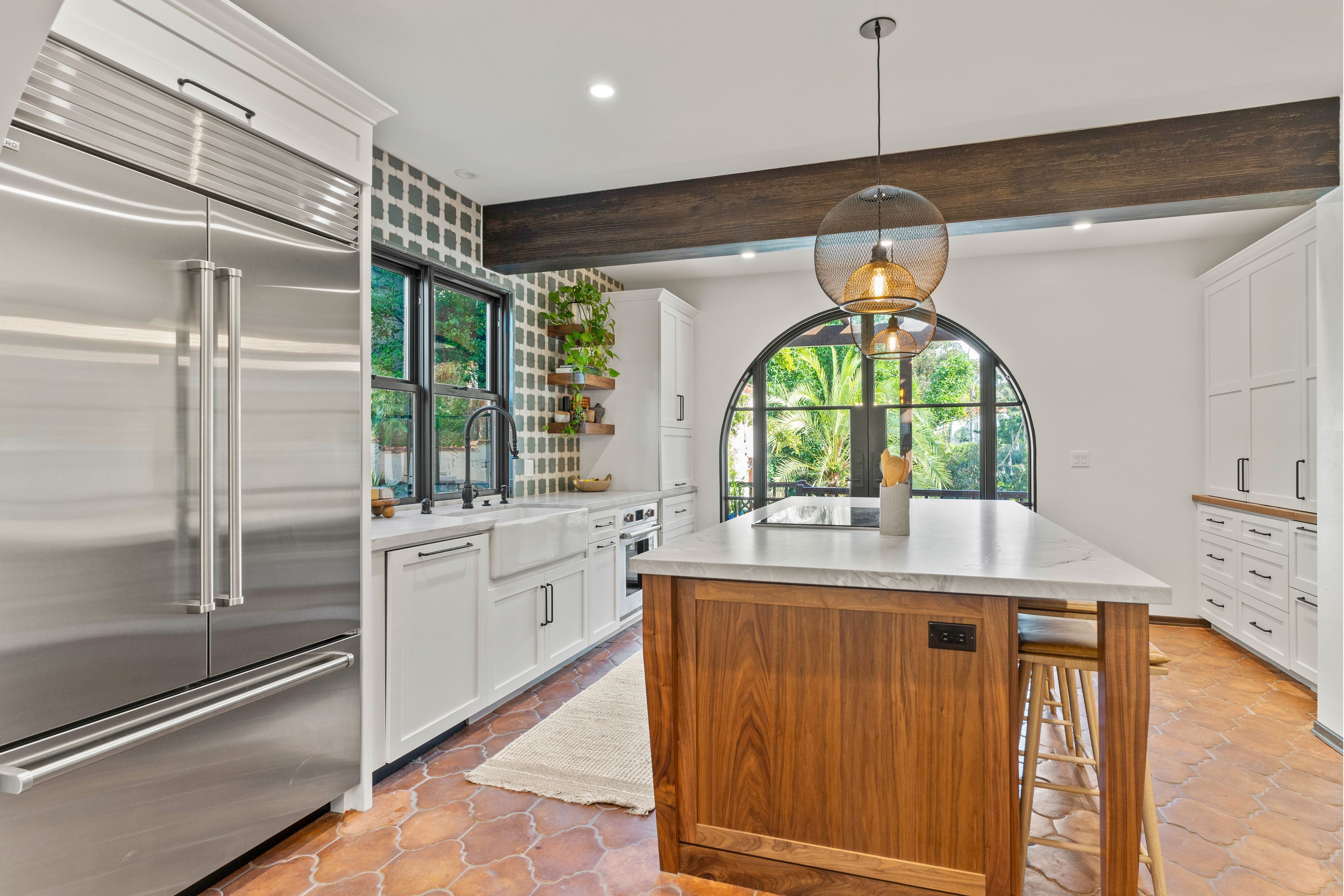 White kitchen with wood island, apron-front sink, patterned tile, arched rear doors and stainless appliances.