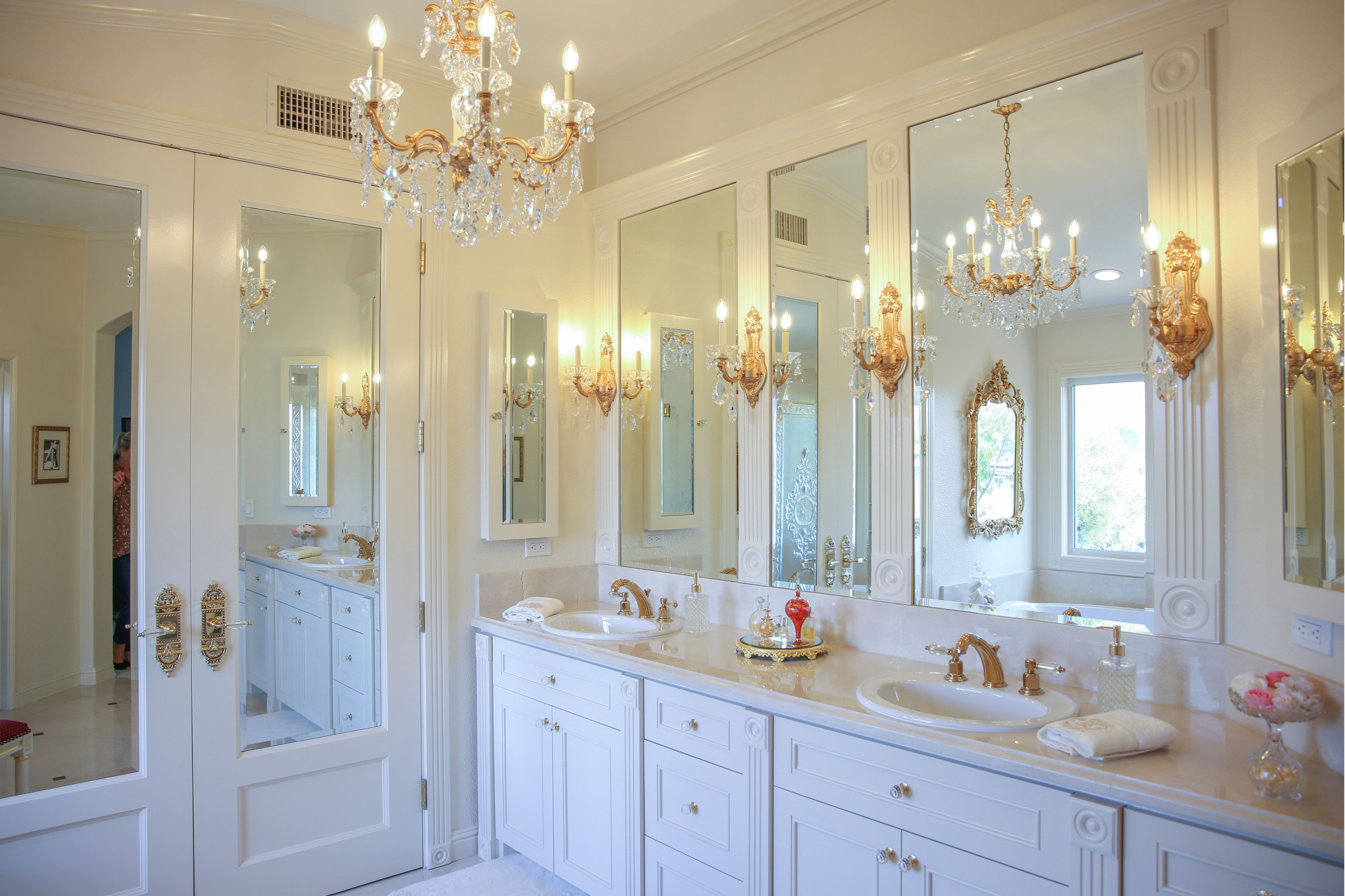 Carlsbad master bath with double vanity, marble counters, ornate millwork, gold crystal sconces and chandelier.