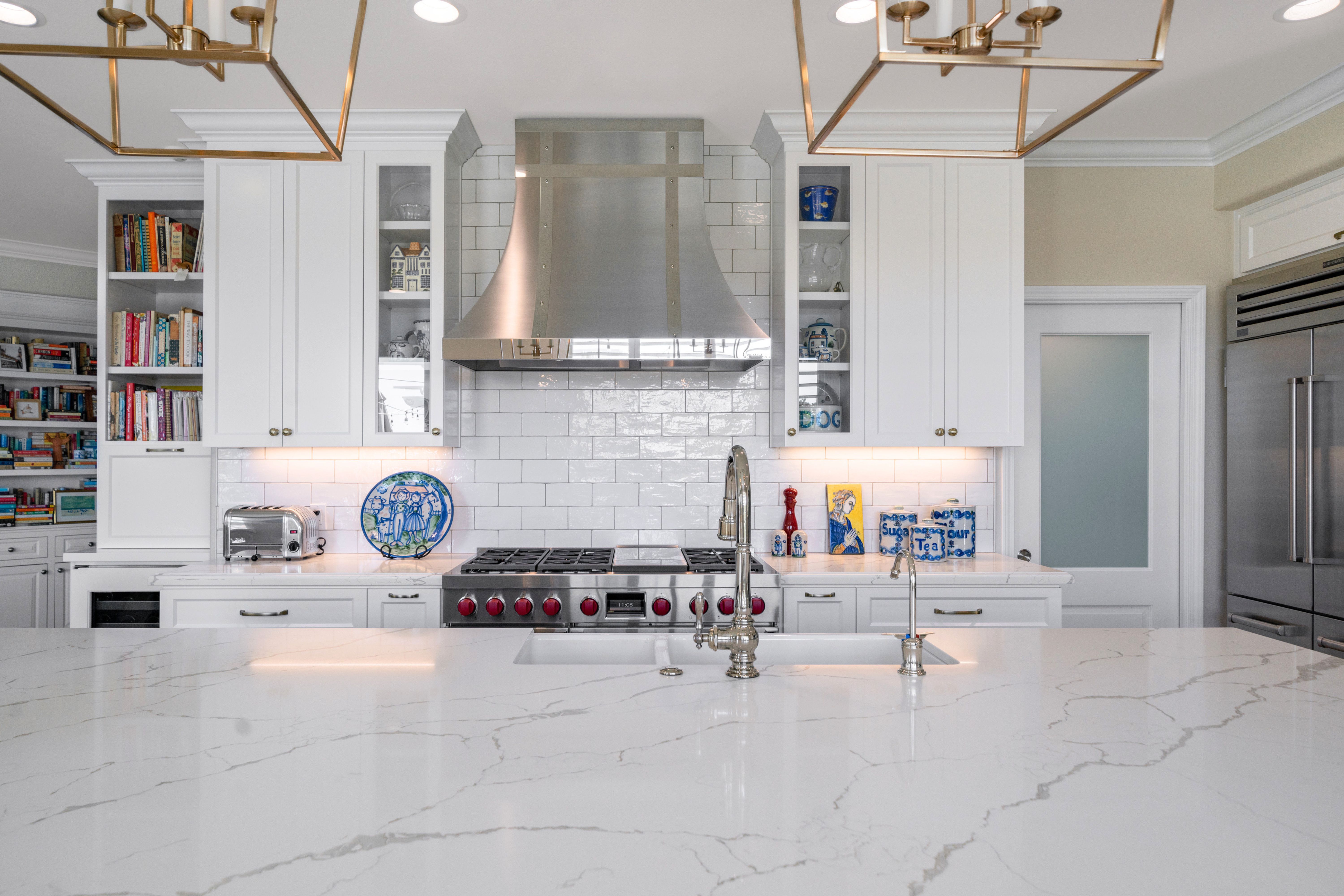Two-cook kitchen with an expanded veined island, white cabinetry, stainless range and oversized hood.