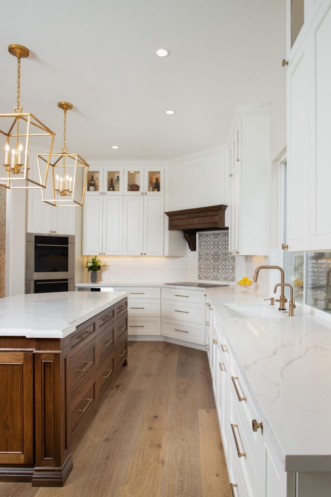 Carlsbad kitchen remodel with dark wood island, white cabinetry, veined counters, brass pendants and apron-front sink.