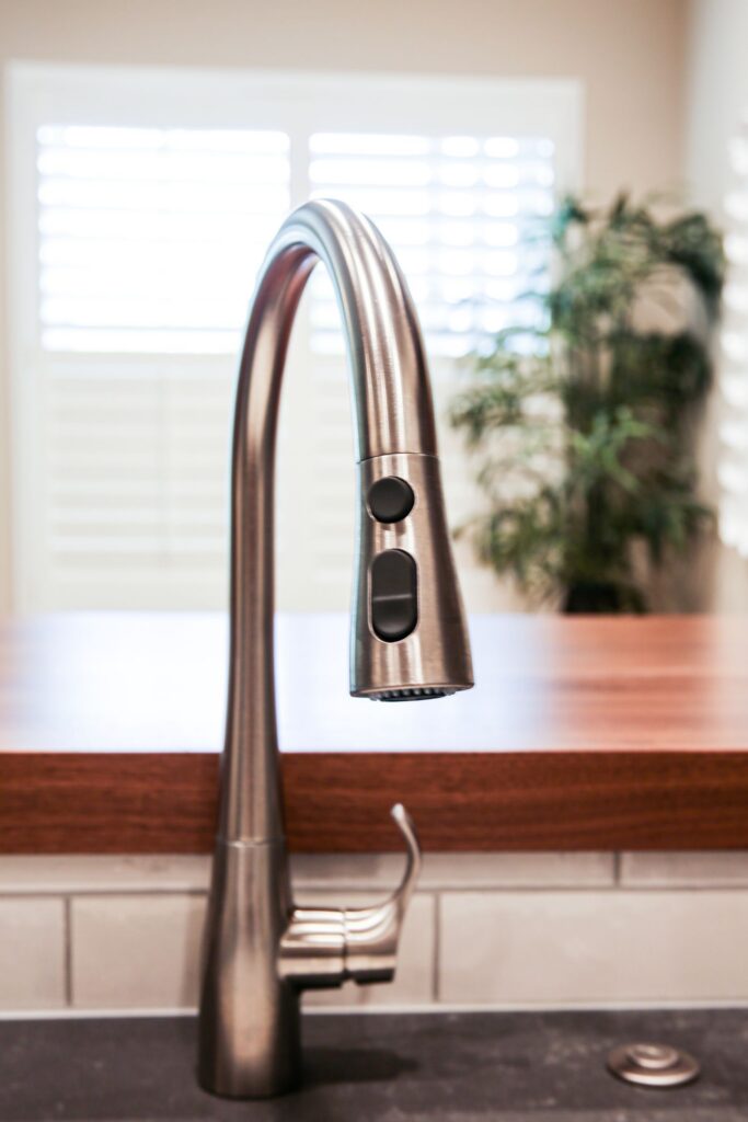 Brushed stainless pull-down kitchen faucet with gray countertop, wood ledge and white subway tile backsplash