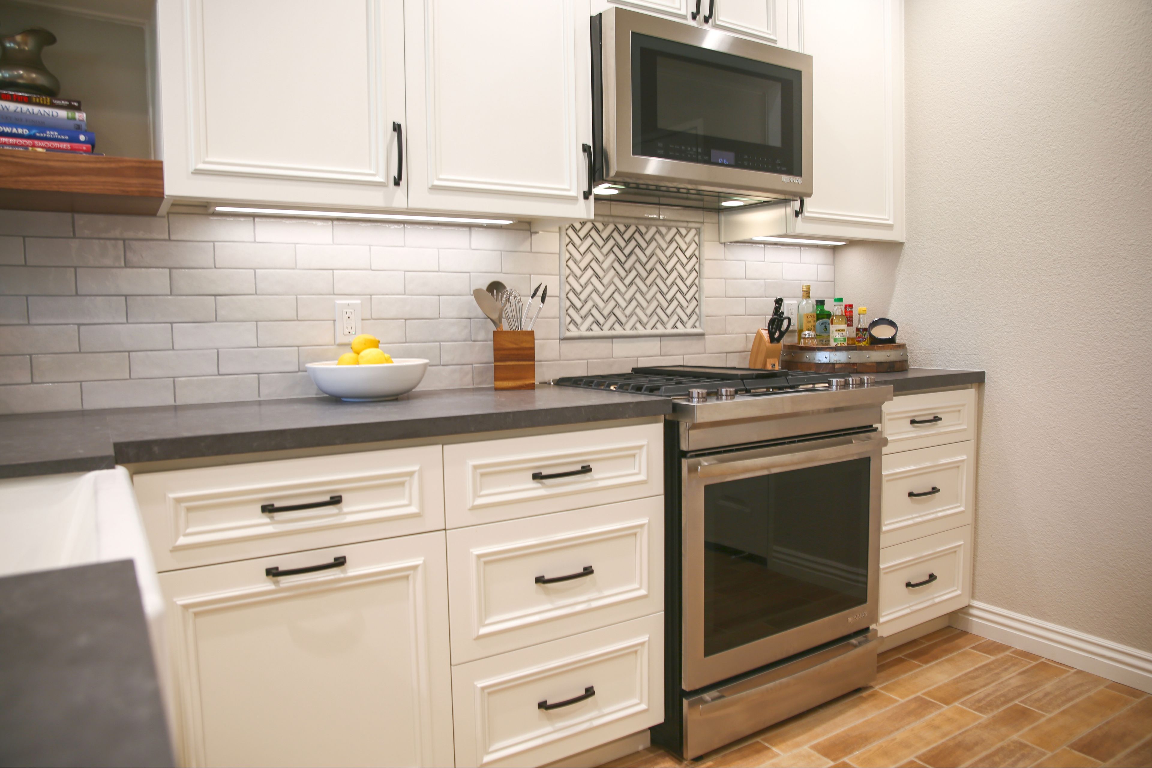 White kitchen cabinetry with stainless gas range, microwave hood, gray counters and herringbone tile accent