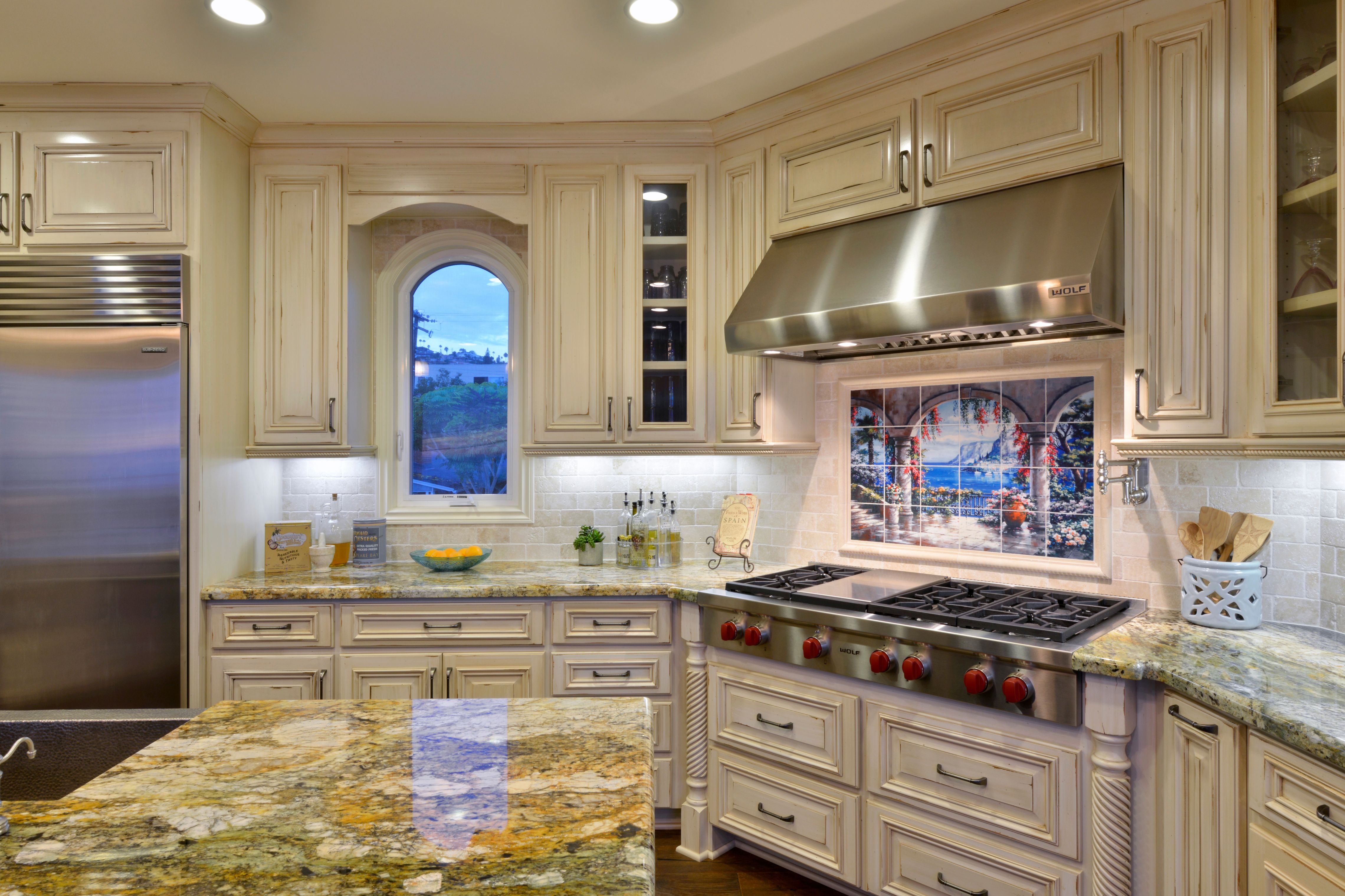 Kitchen remodel with cream cabinetry, granite counters, stainless range and hood, arched window and tile backsplash.