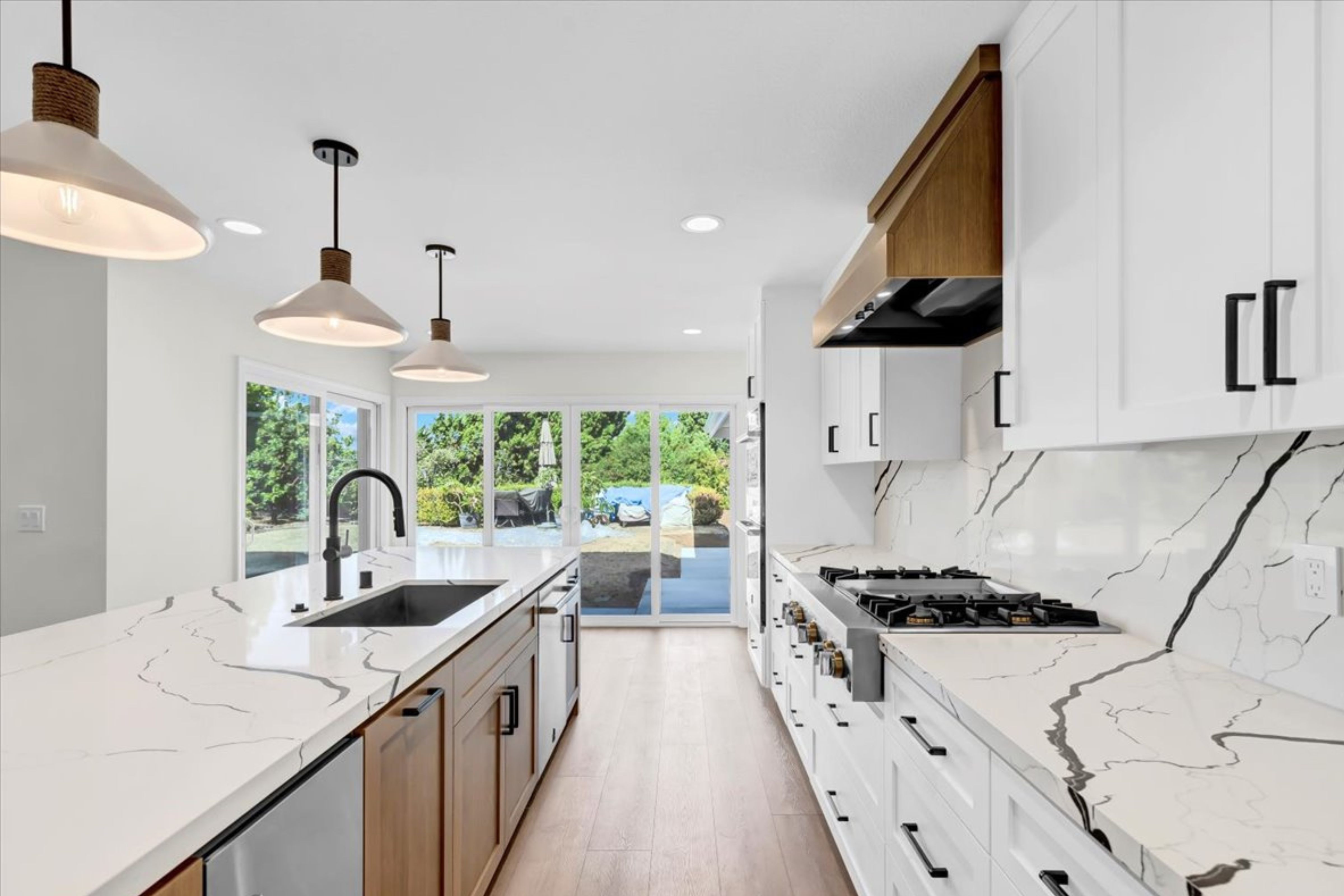 Kitchen with wood island cabinetry, white perimeter cabinets, stainless appliances, slab backsplash and pendant lighting.