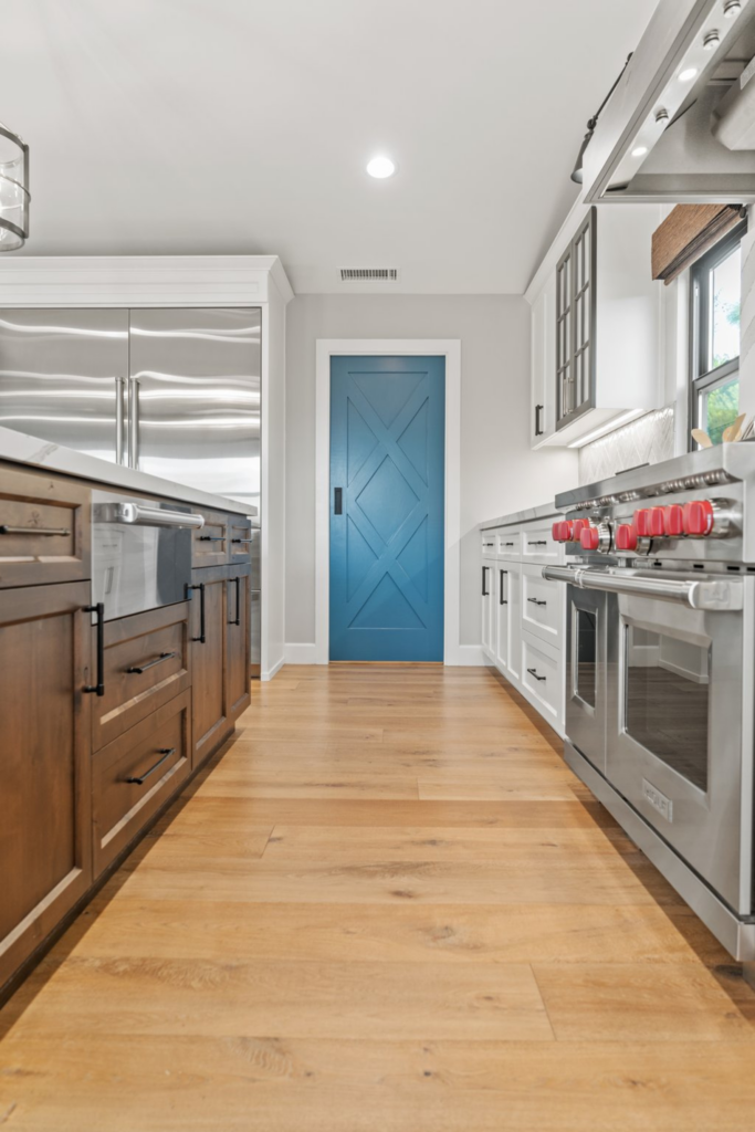 Encinitas kitchen remodel with wood island cabinetry, white cabinets, stainless appliances, blue pantry door and wood flooring.