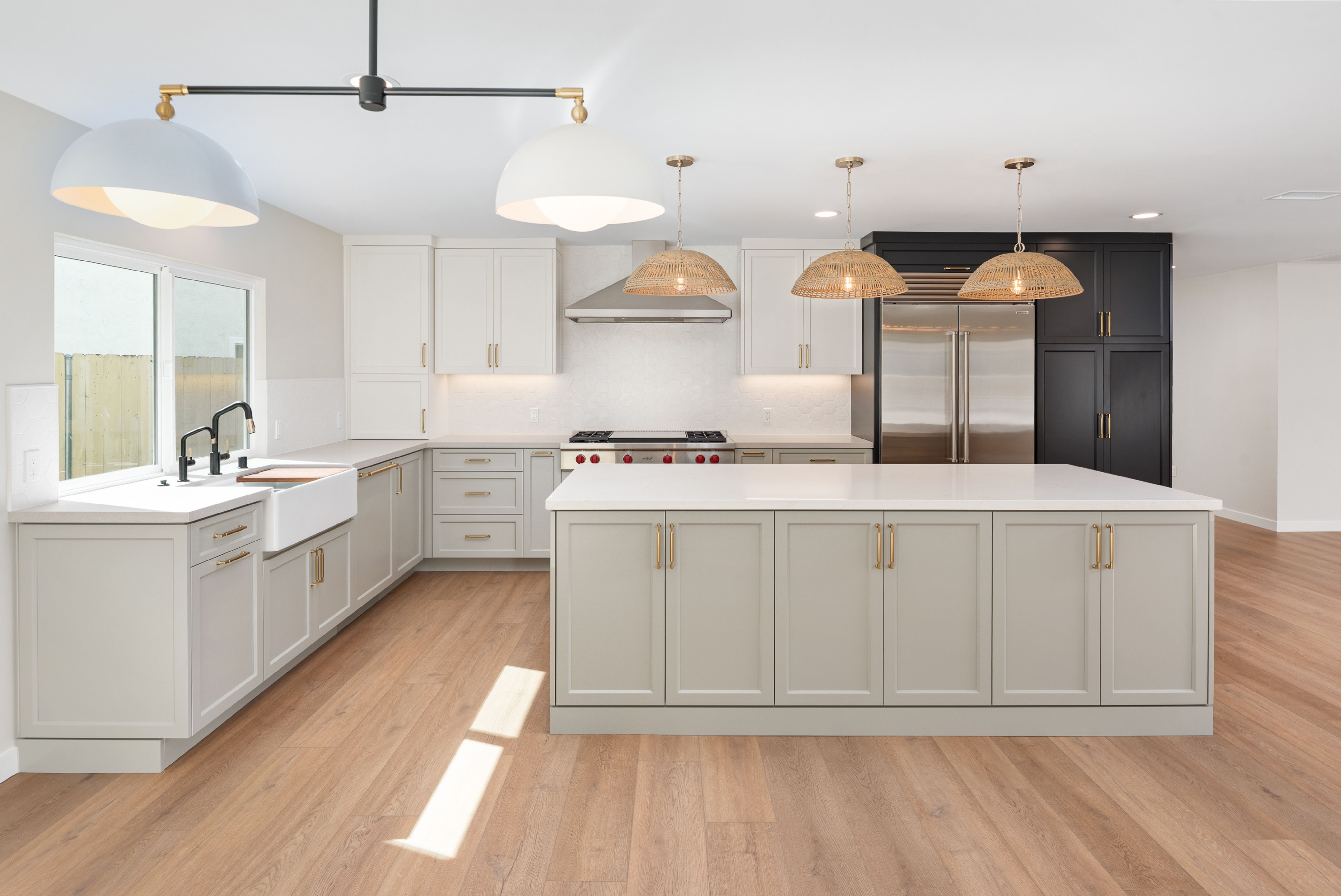Open kitchen with large island, white cabinetry, black pantry cabinets, farmhouse sink and woven pendant lights.