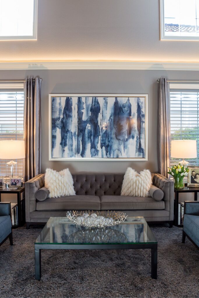 Two-story living room with gray sofa, blue chairs, clerestory windows, cove lighting and light wood flooring.