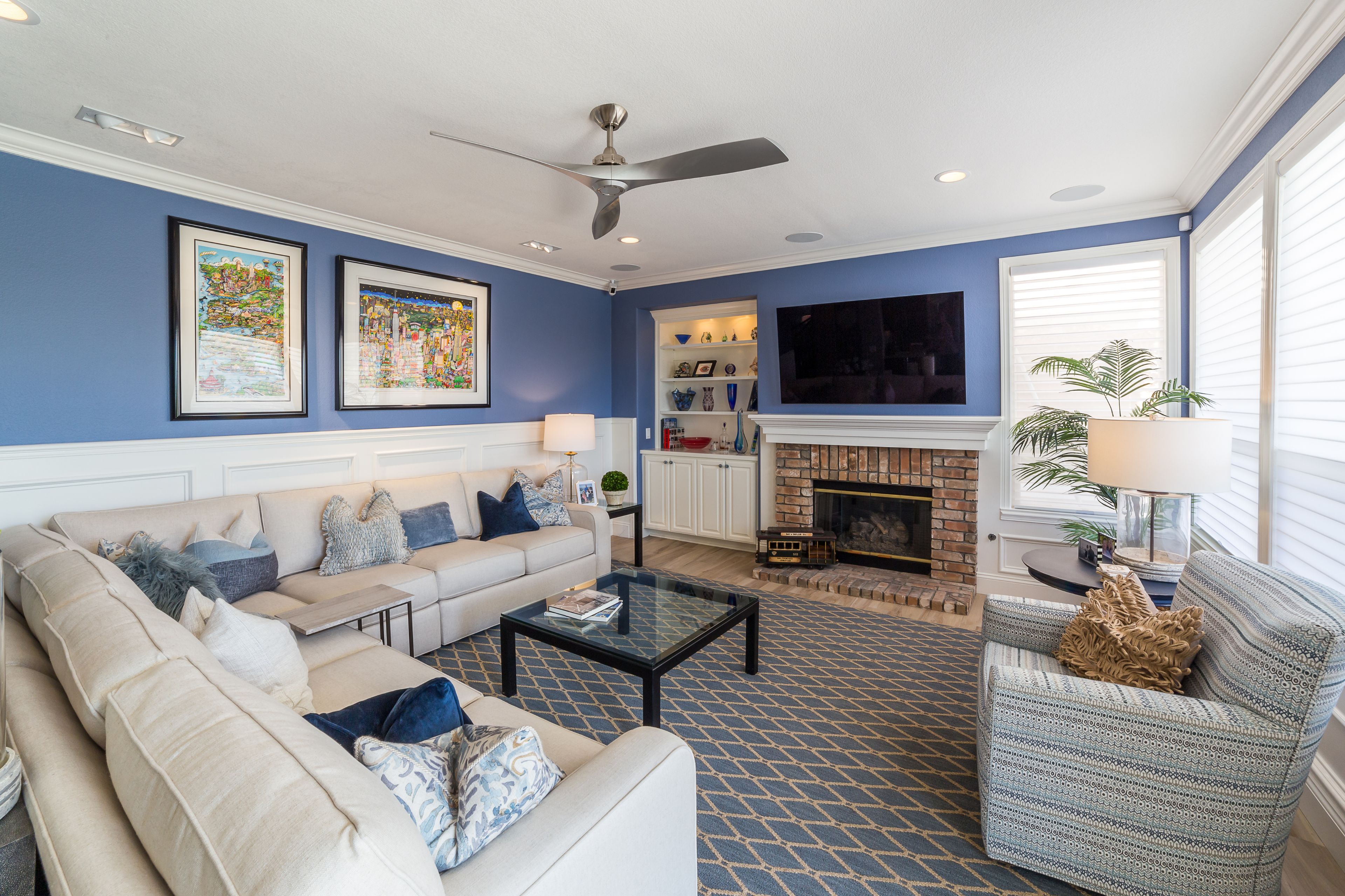 Family room with blue walls, white wainscoting, brick fireplace, built-in cabinetry and large windows.