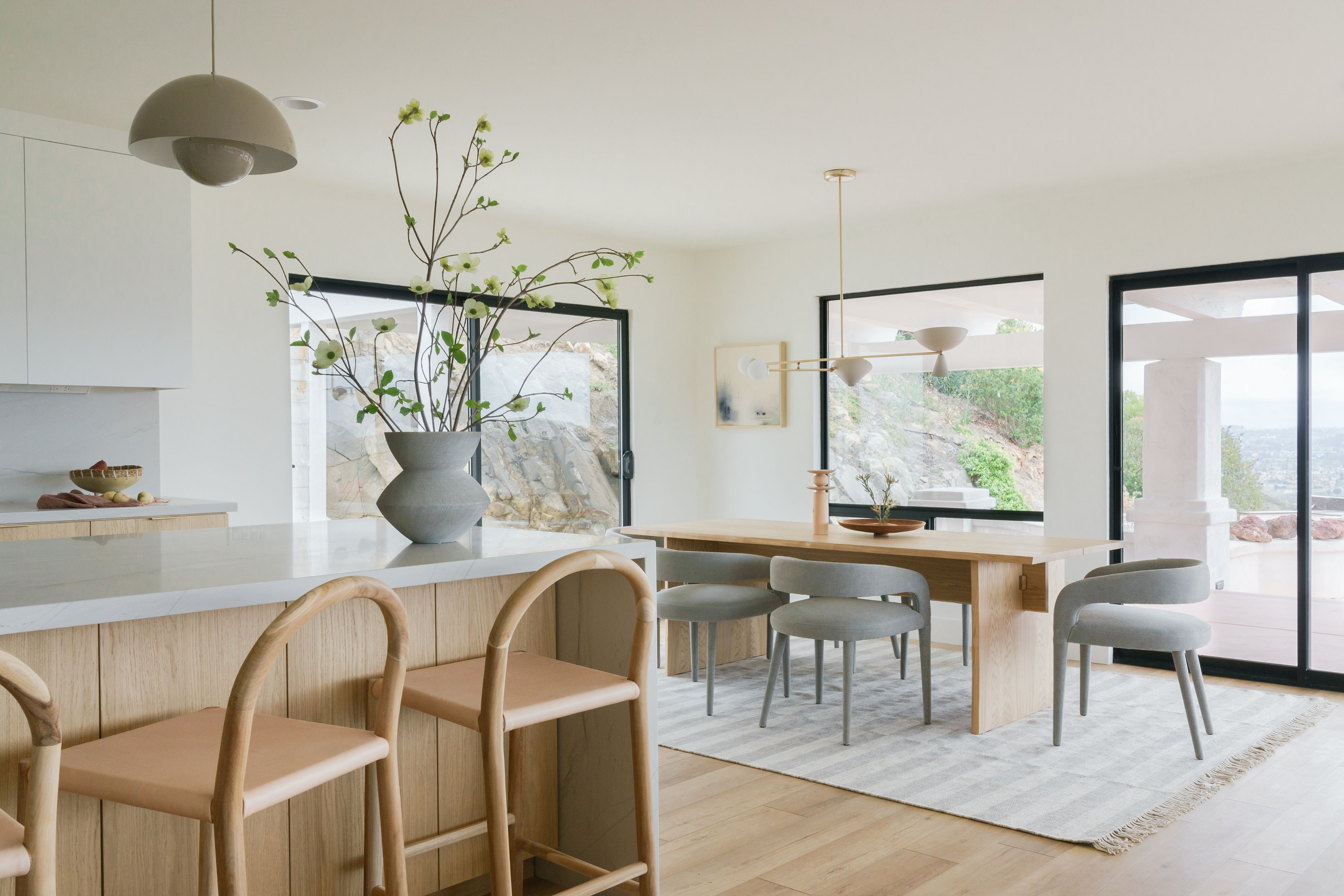 Open-concept kitchen and dining area with light wood cabinetry, stone countertops and large dark-framed windows