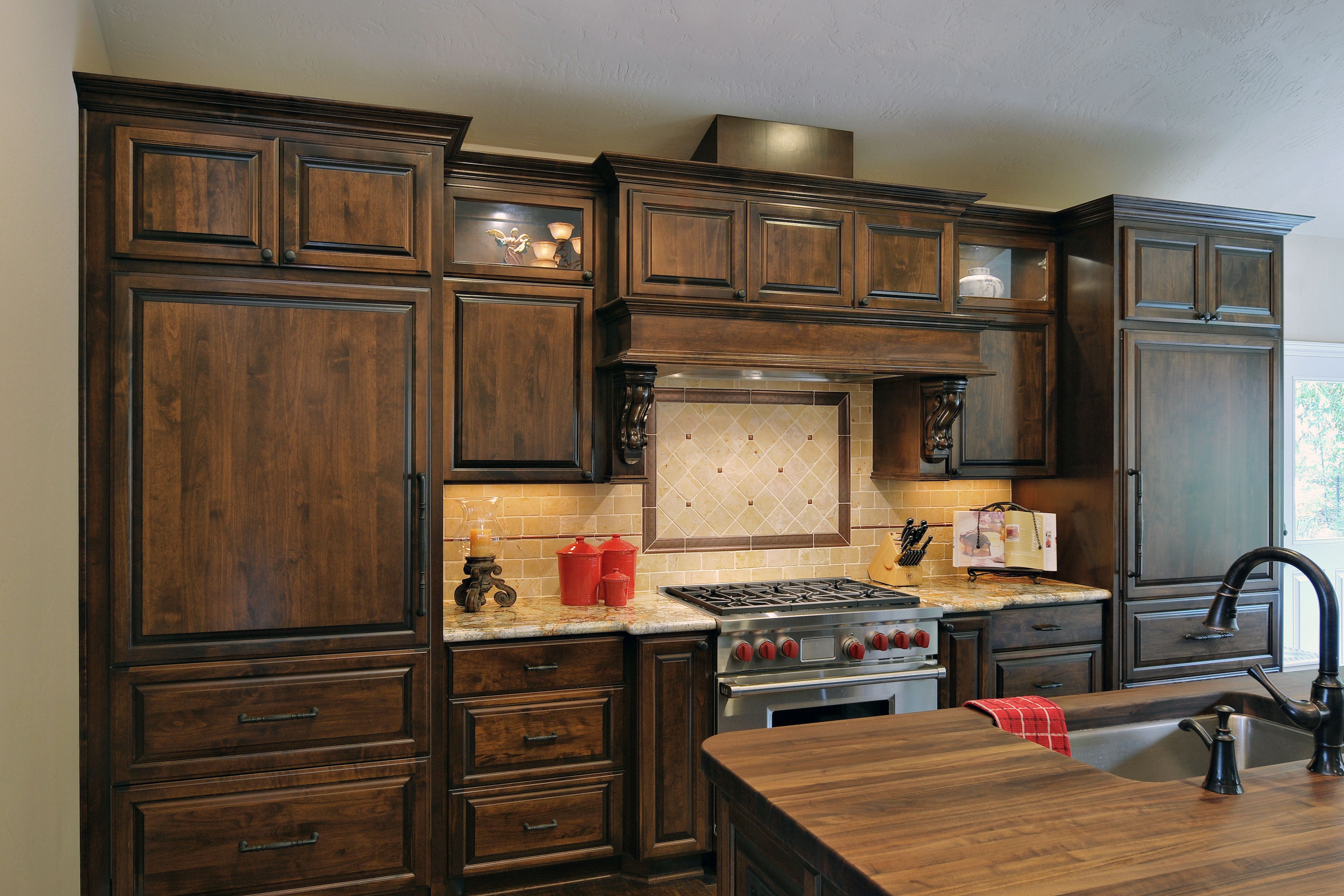 Dark-stained kitchen cabinetry with pro-style range, tiled backsplash and walnut-topped island sink