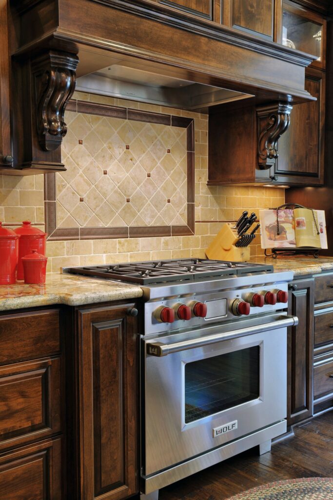 Dark wood kitchen cabinetry with stainless range, carved wood hood and decorative stone tile backsplash