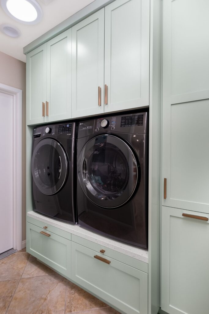 Laundry room with stacked cabinetry around front-load washer and dryer, mint-green finish and brass hardware