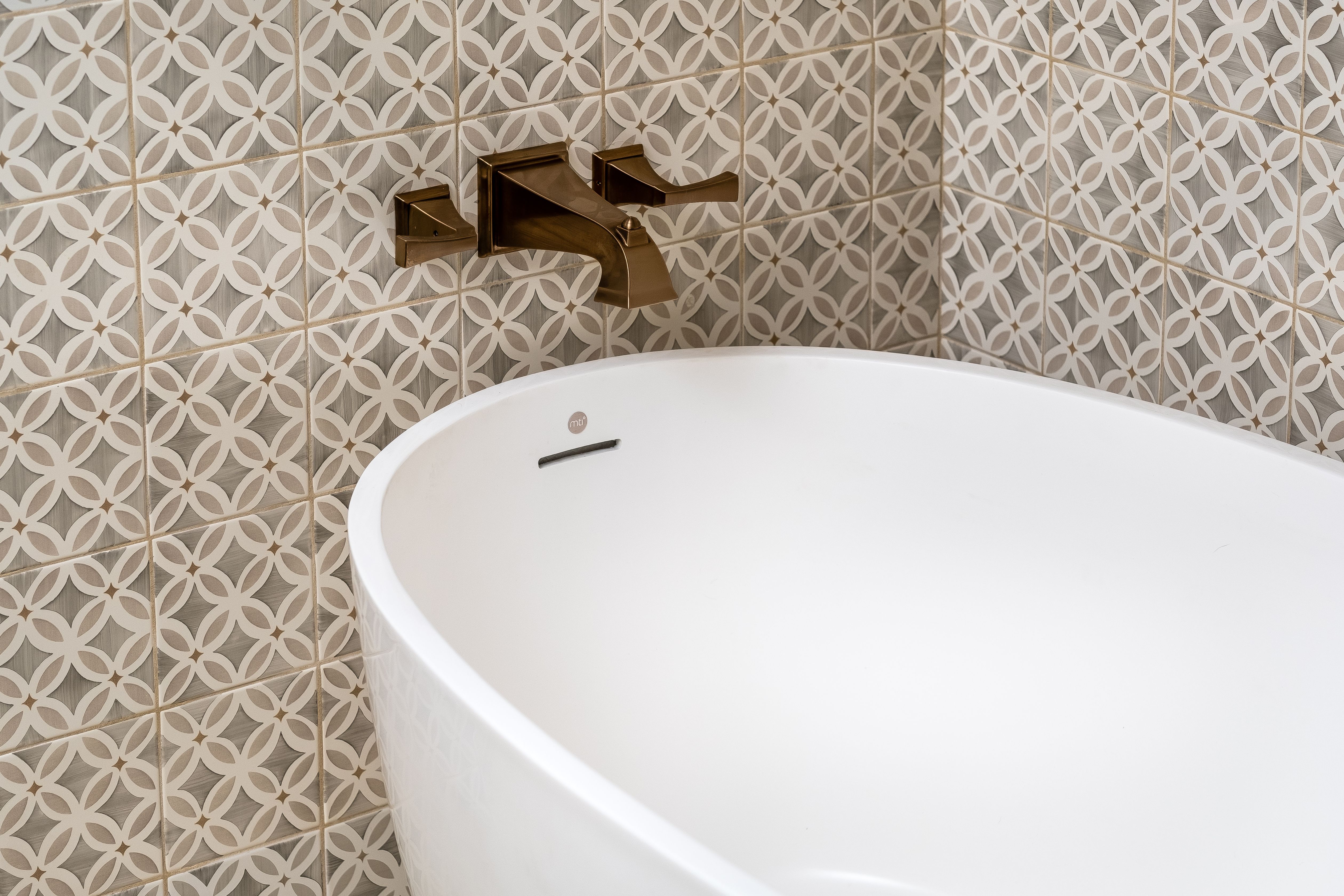 Soaking tub with patterned tile surround and wall-mounted bronze tub filler