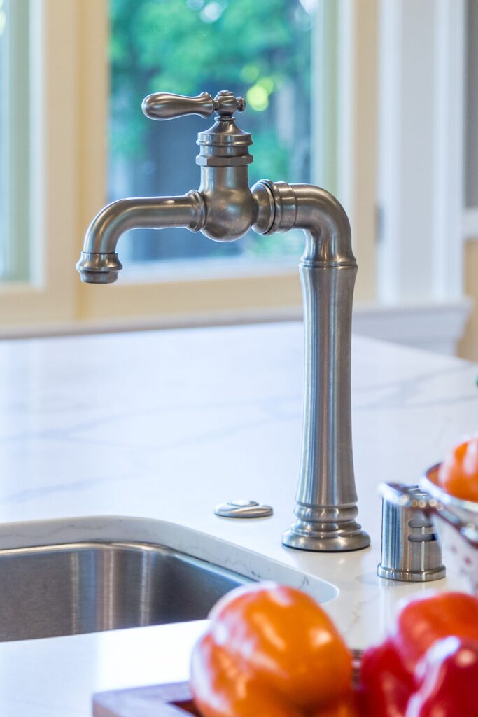 Brushed nickel kitchen faucet beside stainless sink and white countertop with garden-facing window