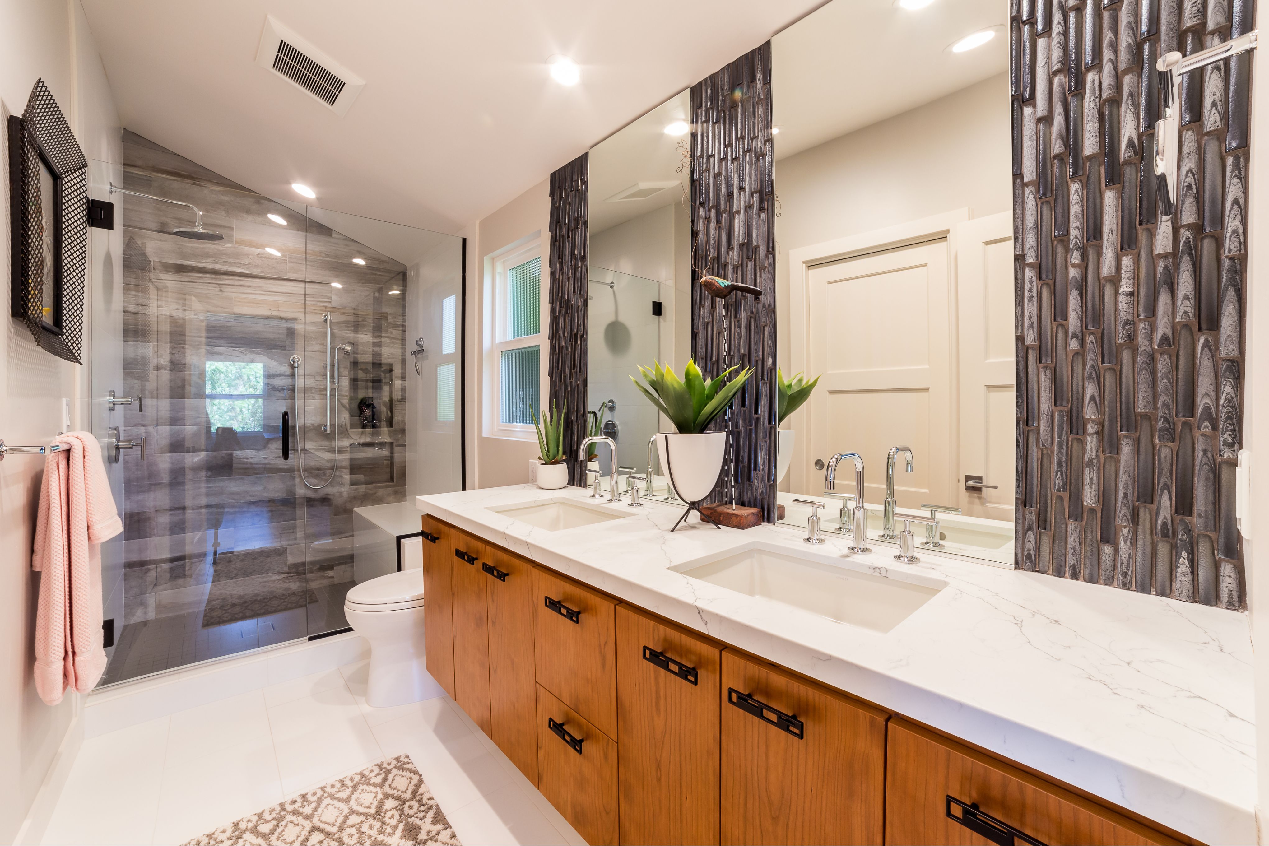 Primary bathroom with double wood vanity, veined white countertop, large mirrors and glass-enclosed tiled shower