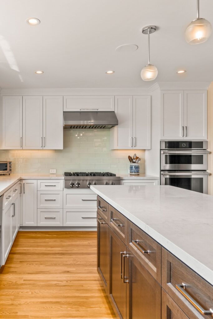 Kitchen with white shaker cabinetry, dark wood island, light counters, pendant lighting and hardwood floors