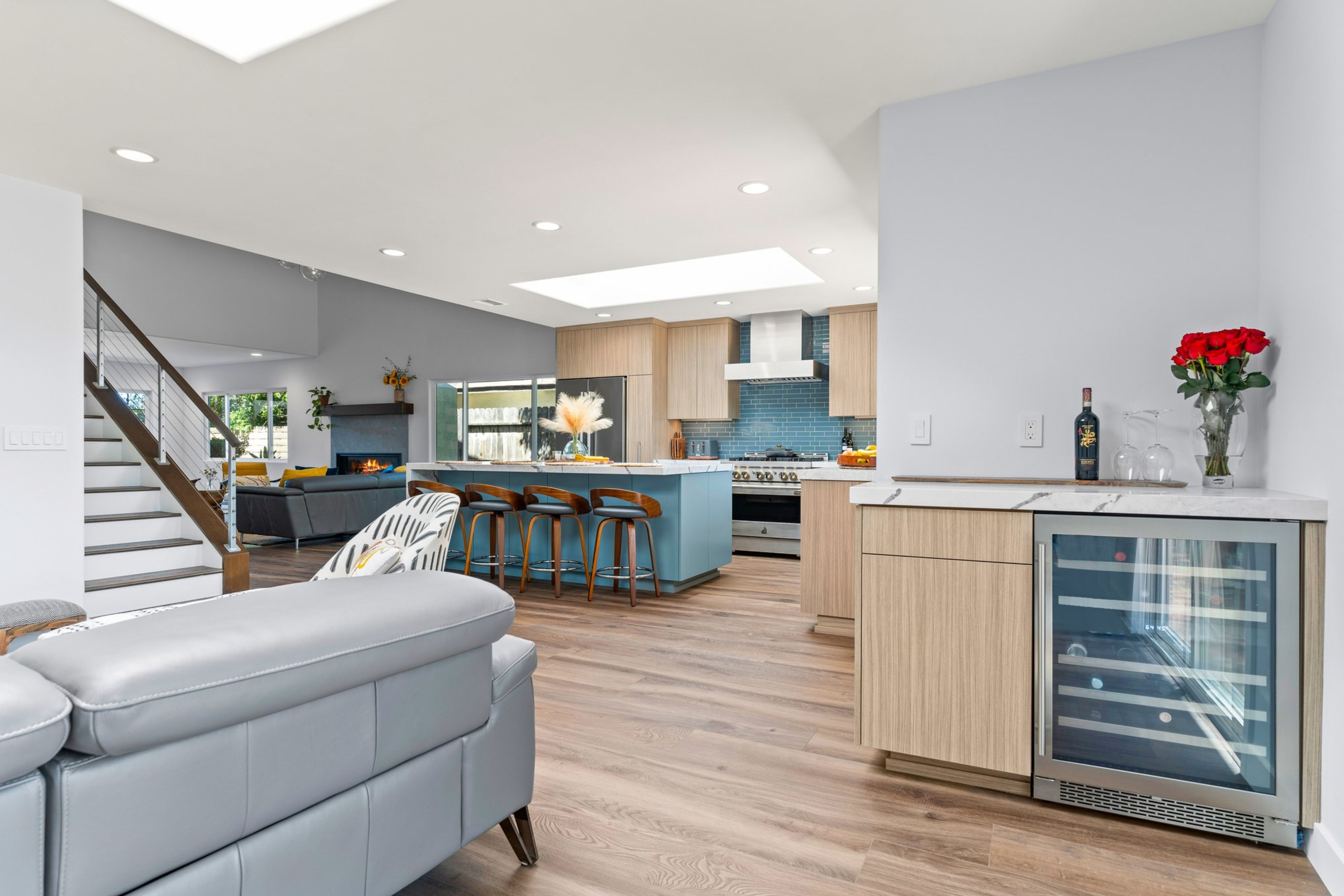 Open Del Mar kitchen with blue island, light wood cabinetry, cable-railed stairs, skylights and built-in beverage fridge.