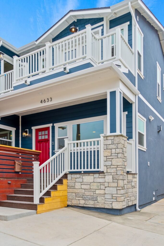 Ocean Beach exterior with blue siding, red entry door, stone veneer, white railings and second-floor deck.