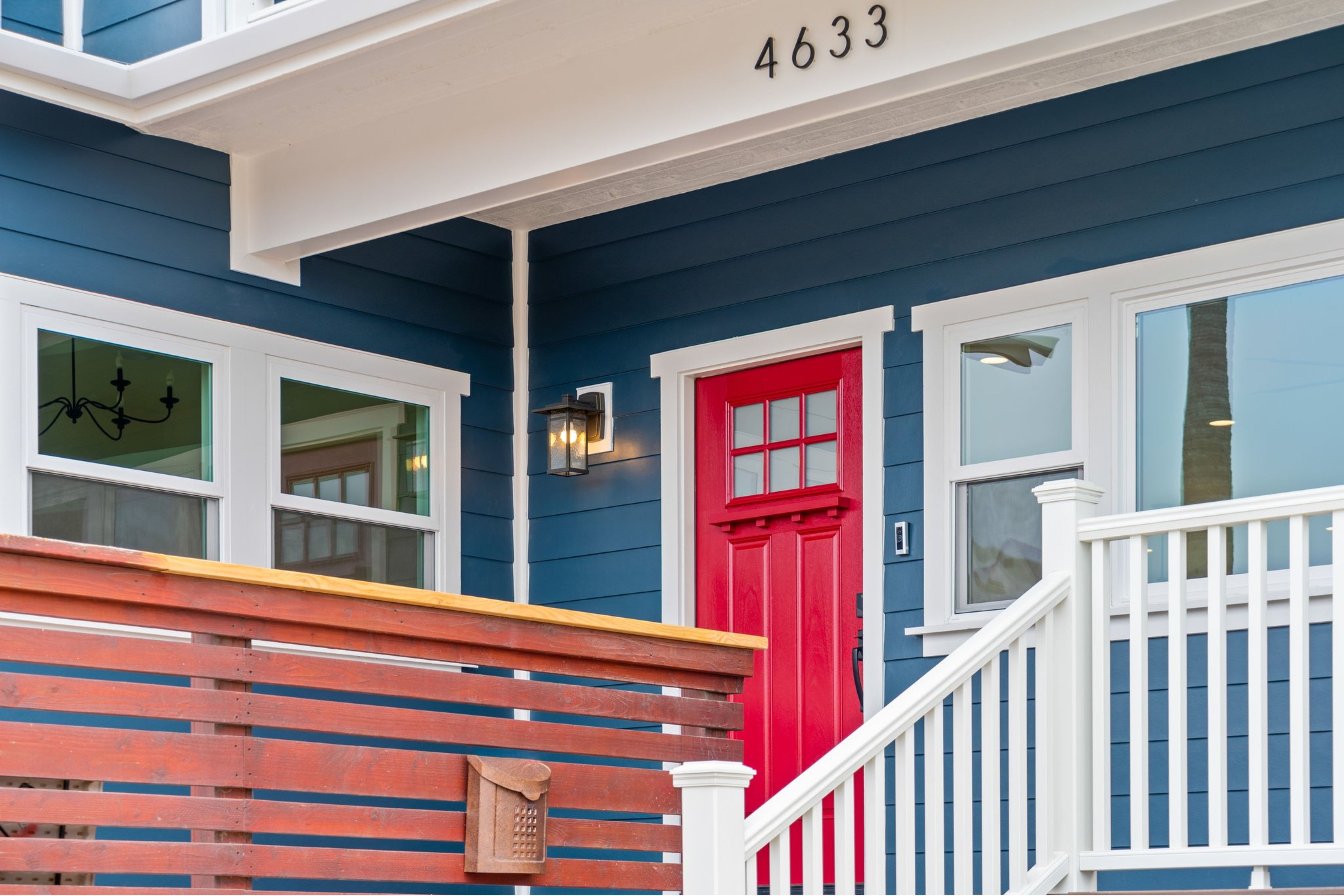 Ocean Beach entry with blue siding, red front door, white trim, wood railing and covered porch.