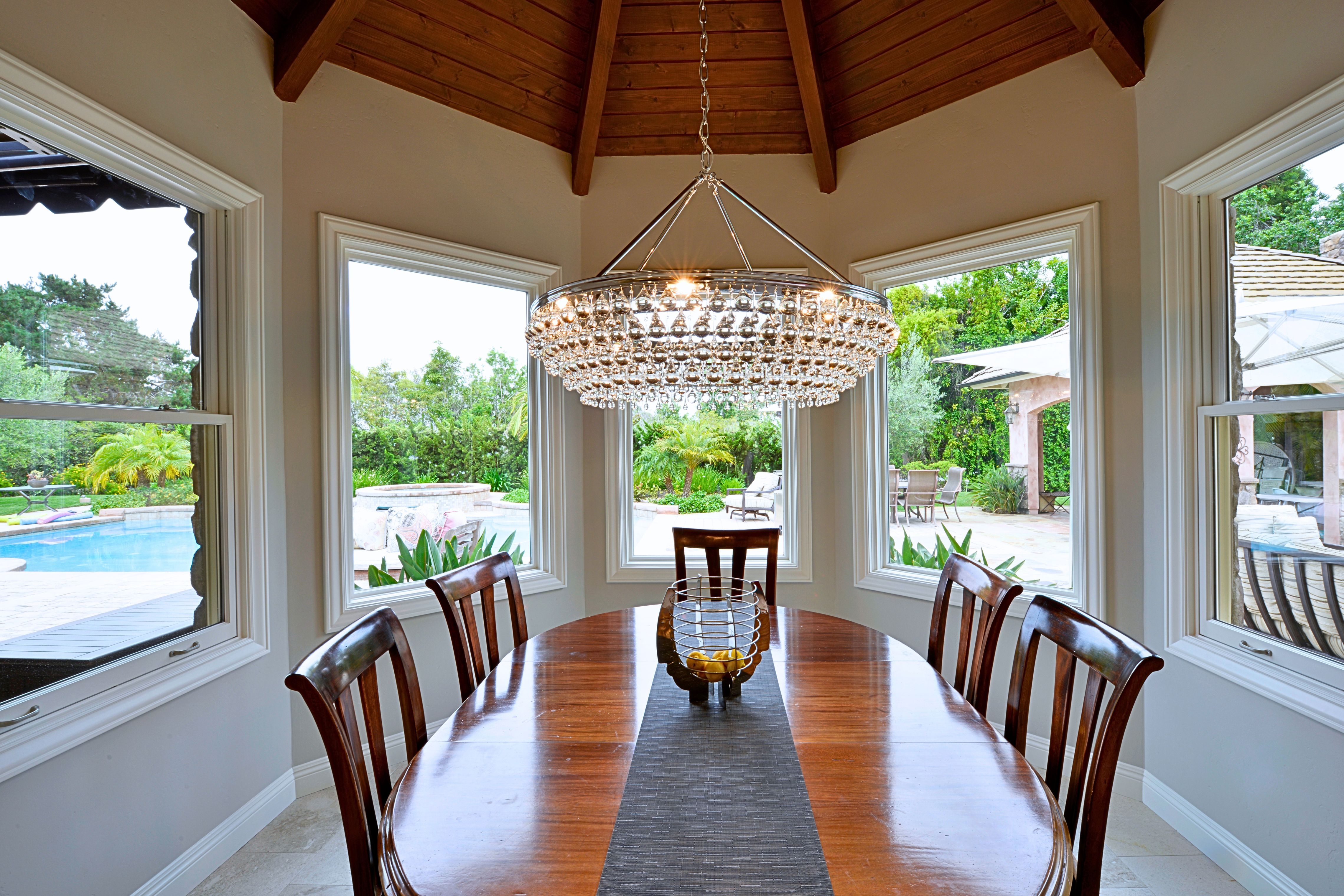 Del Mar dining nook with wood-plank vaulted ceiling, exposed beams, crystal chandelier and large windows overlooking the patio.