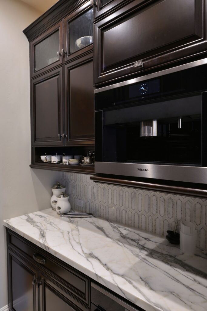 Dark wood pantry cabinetry with built-in coffee system, marble-look counter and geometric tile backsplash